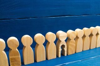 Foto: Holzfiguren in einer Reihe, eine hat ein ausgeschnittenes Kind